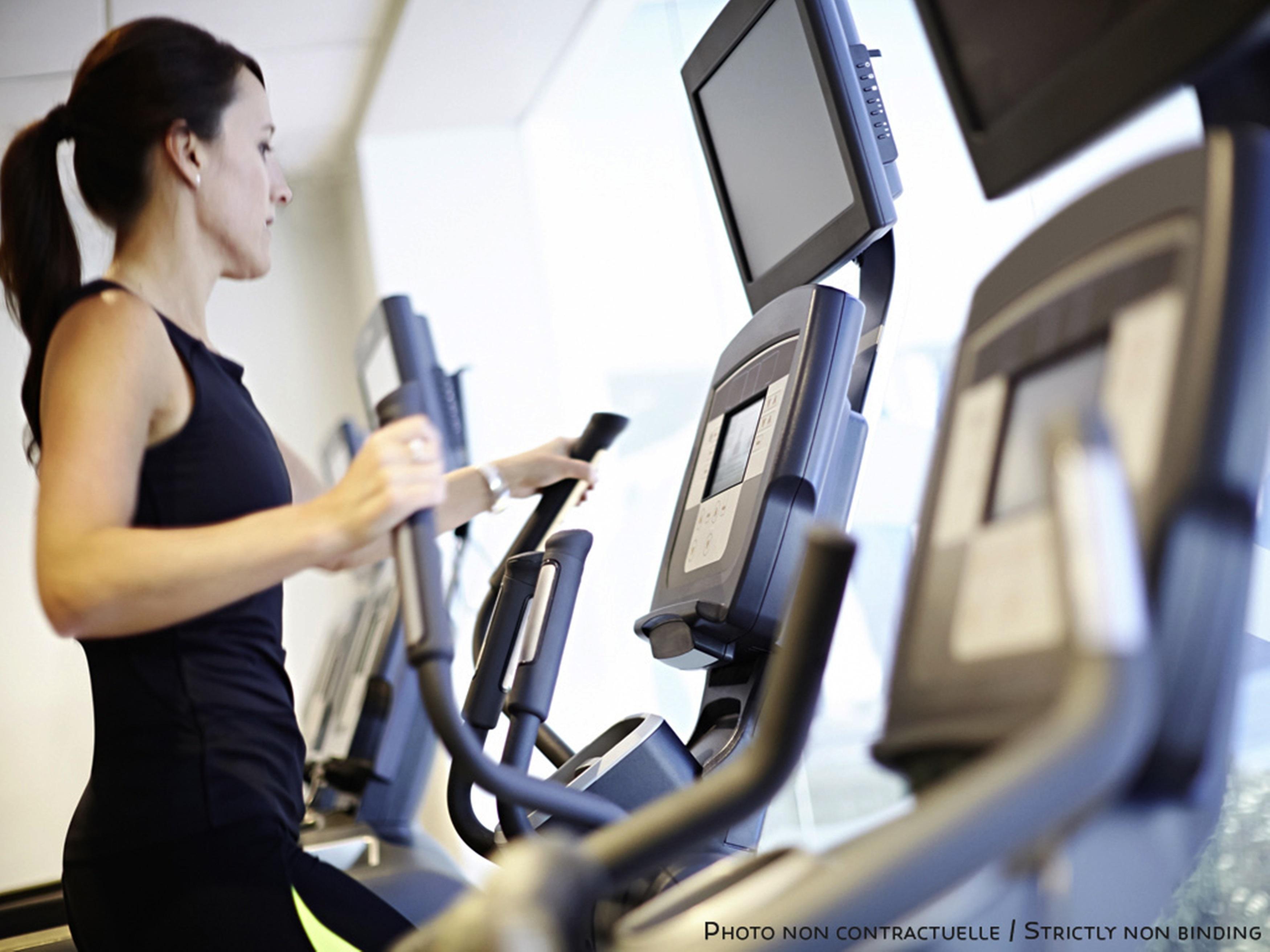 Novotel New Delhi Aerocity Buitenkant foto The photo shows a woman using elliptical machines in a gym or fitness center. She appears focused on her workout, dressed in athletic clothing. The machines feature digital screens, likely displaying workout statistics or options. The environment is 
