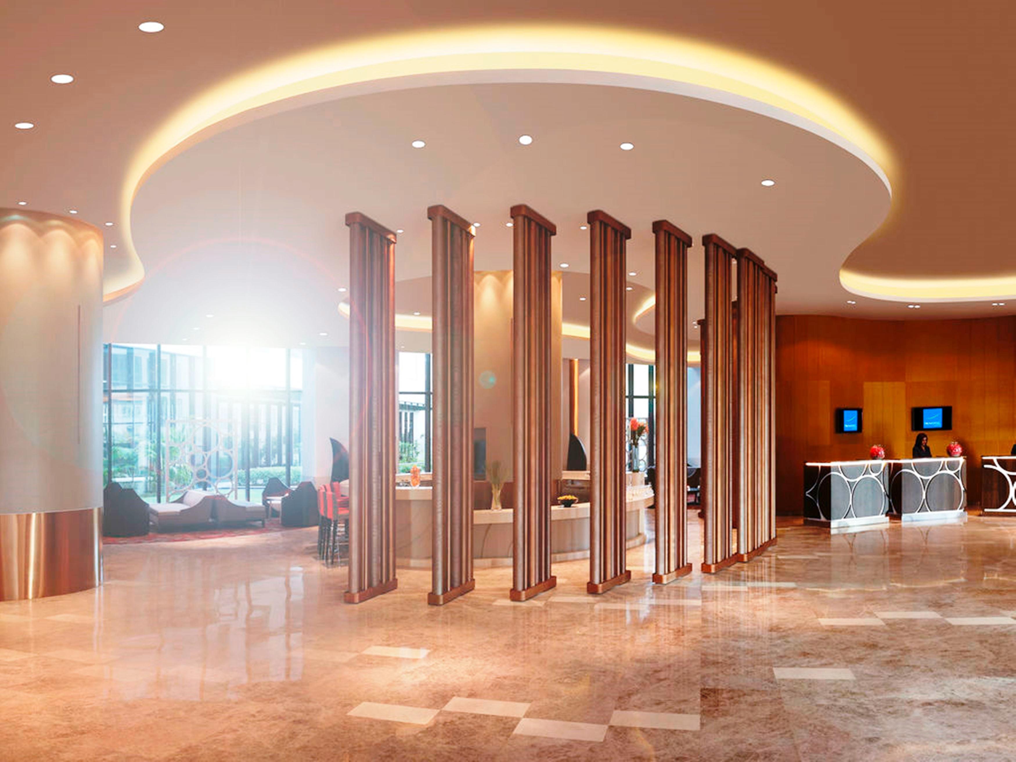 Novotel New Delhi Aerocity Buitenkant foto The photo shows the interior of a modern hotel lobby. It features a spacious layout with polished marble flooring and a softly lit ceiling design that has a curved shape. There are several tall, elegant columns creating a partition, along with a rece